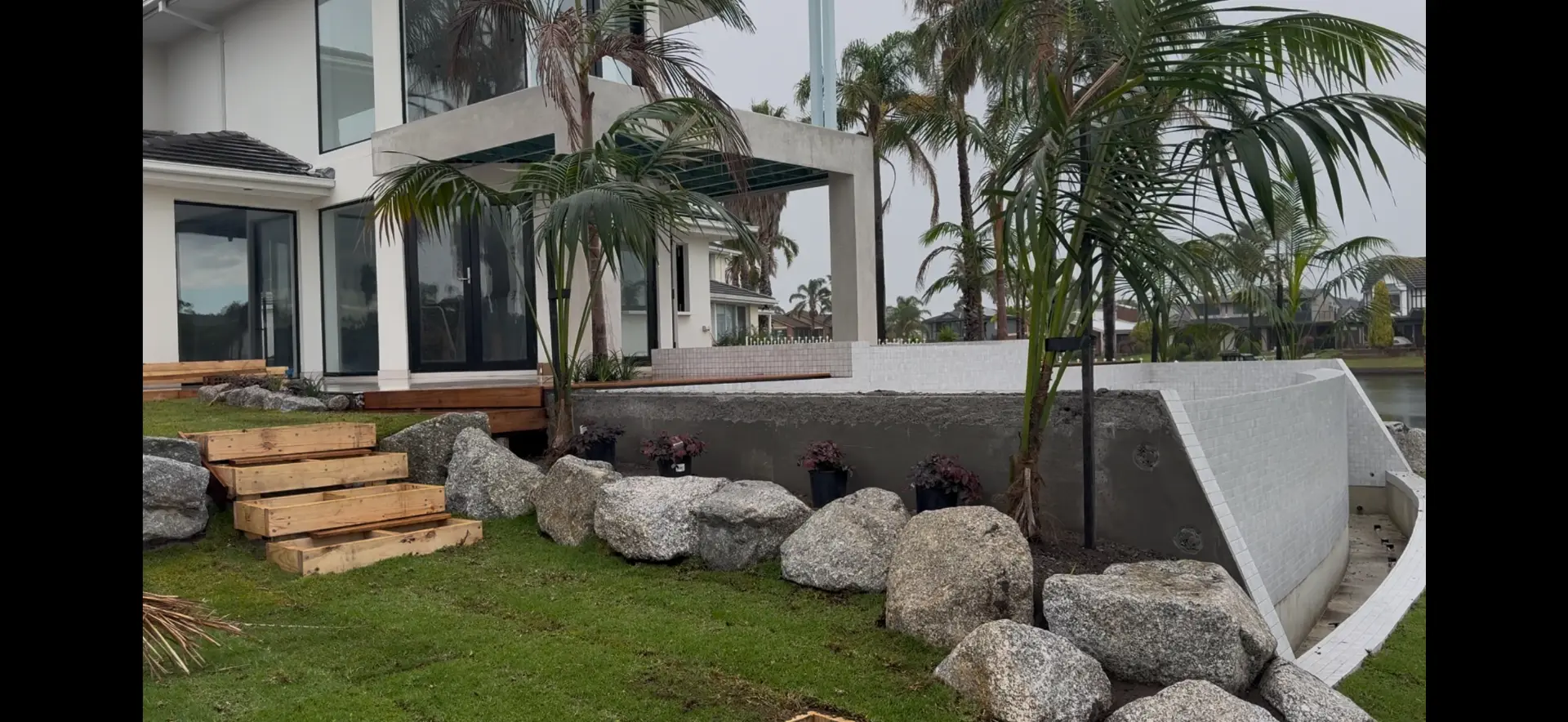 Landscaped waterfront garden with palms, boulders and timber steps